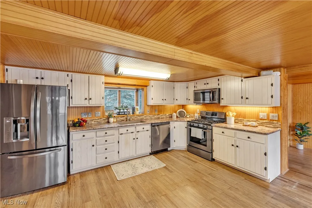 Kitchen featuring stainless steel appliances, wooden walls, wood ceiling, light wood-style flooring, and light stone countertops