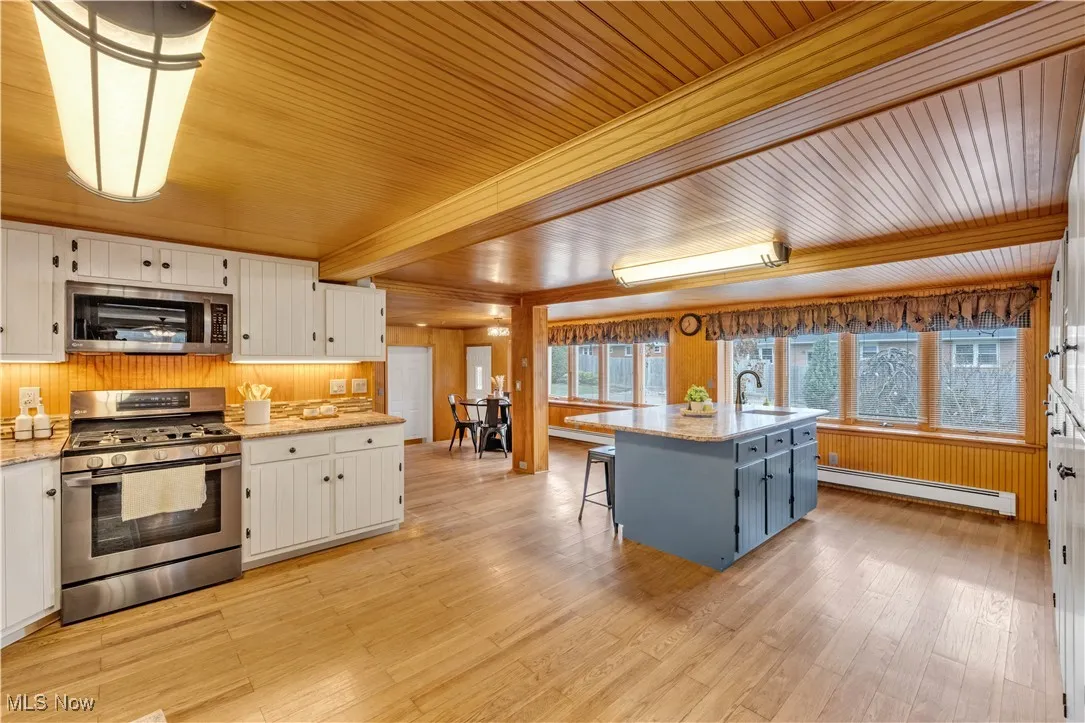Kitchen with stainless steel appliances, wood walls, a breakfast bar area, light stone counters, and a baseboard heating unit
