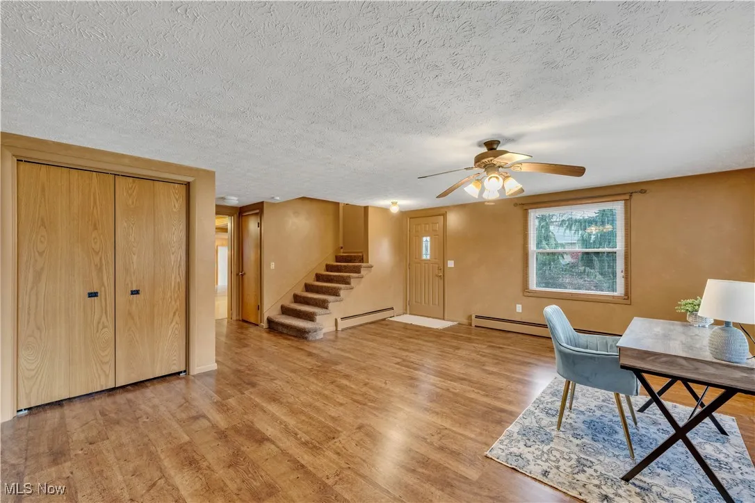 Home office with light wood-style floors, a baseboard radiator, ceiling fan, and a textured ceiling
