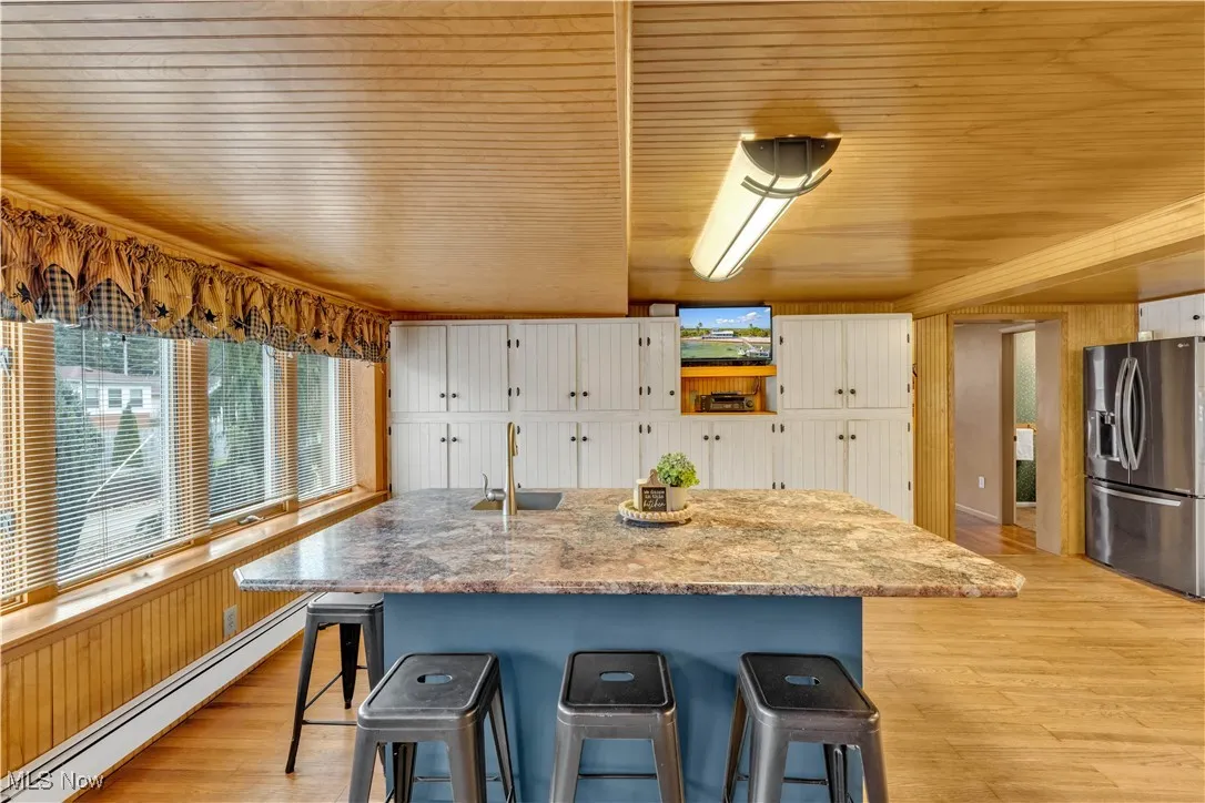 Kitchen featuring baseboard heating, stainless steel fridge with ice dispenser, a breakfast bar area, light wood finished floors, and wood ceiling