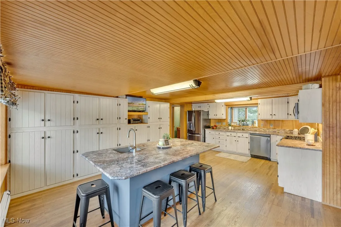 Kitchen featuring wood ceiling, a kitchen bar, light wood-type flooring, appliances with stainless steel finishes, and a kitchen island with sink