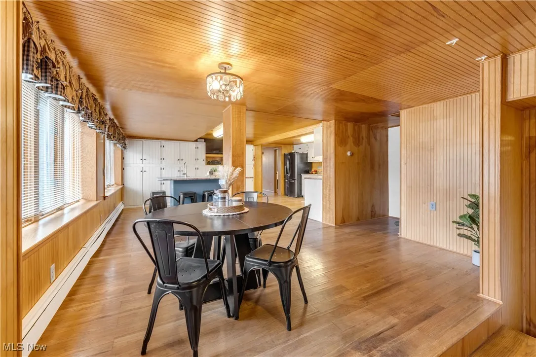 Dining area with wood walls, a baseboard heating unit, wooden ceiling, light wood-style floors, and a chandelier