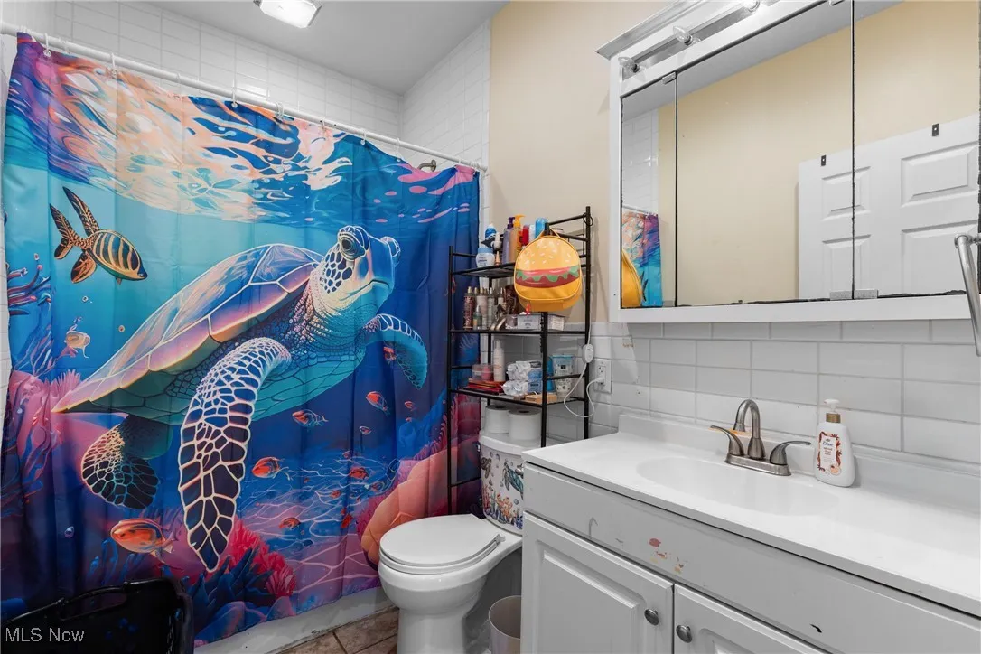 Bathroom featuring vanity, backsplash, and shower / bath combo with shower curtain