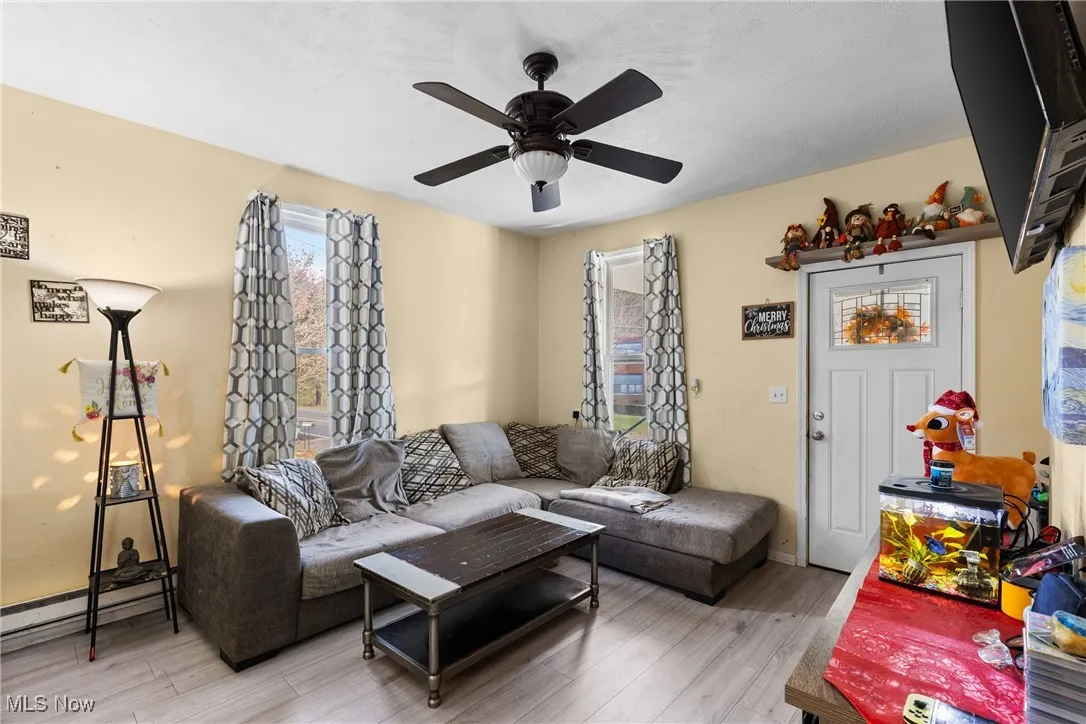 Living room with wood finished floors, a baseboard radiator, and a ceiling fan