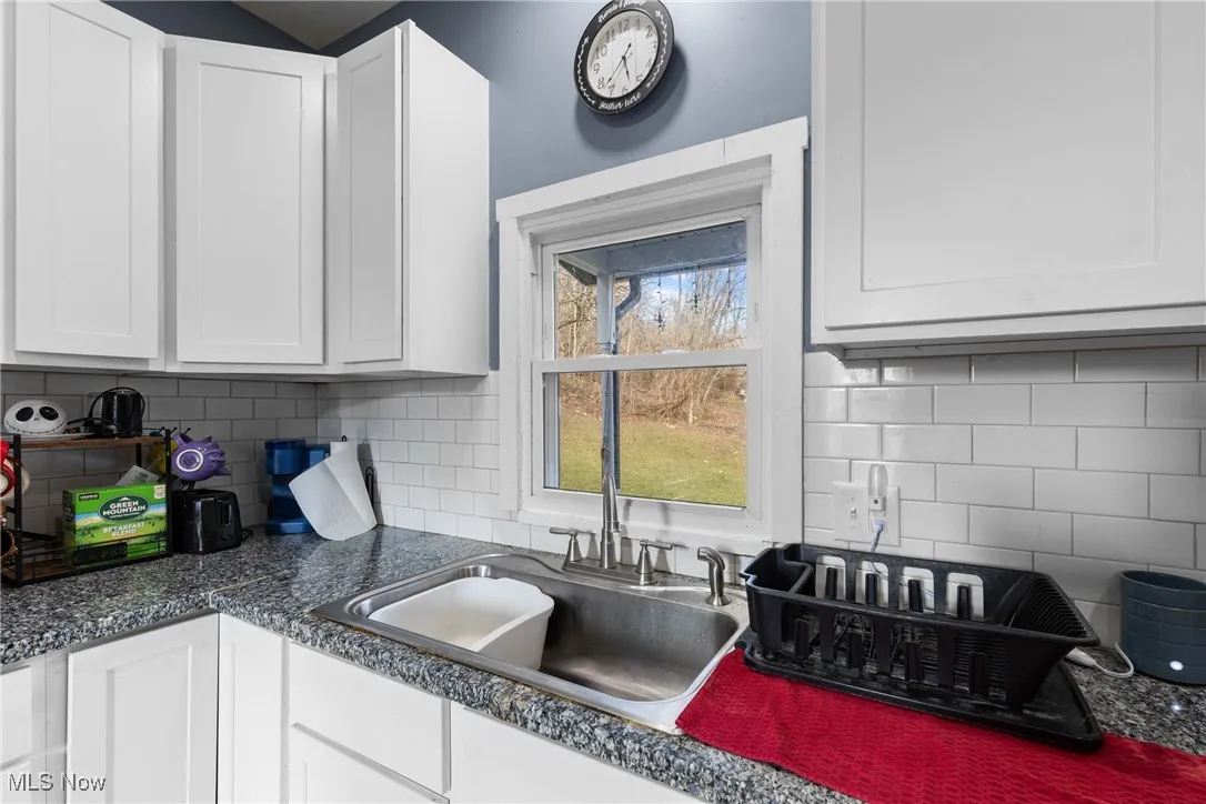 Kitchen with white cabinetry, dark countertops, and tasteful backsplash