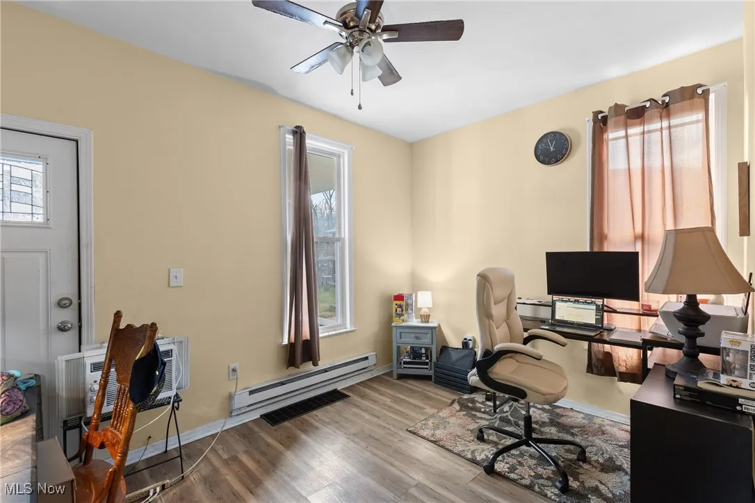 Office with a baseboard heating unit, plenty of natural light, wood finished floors, and a ceiling fan