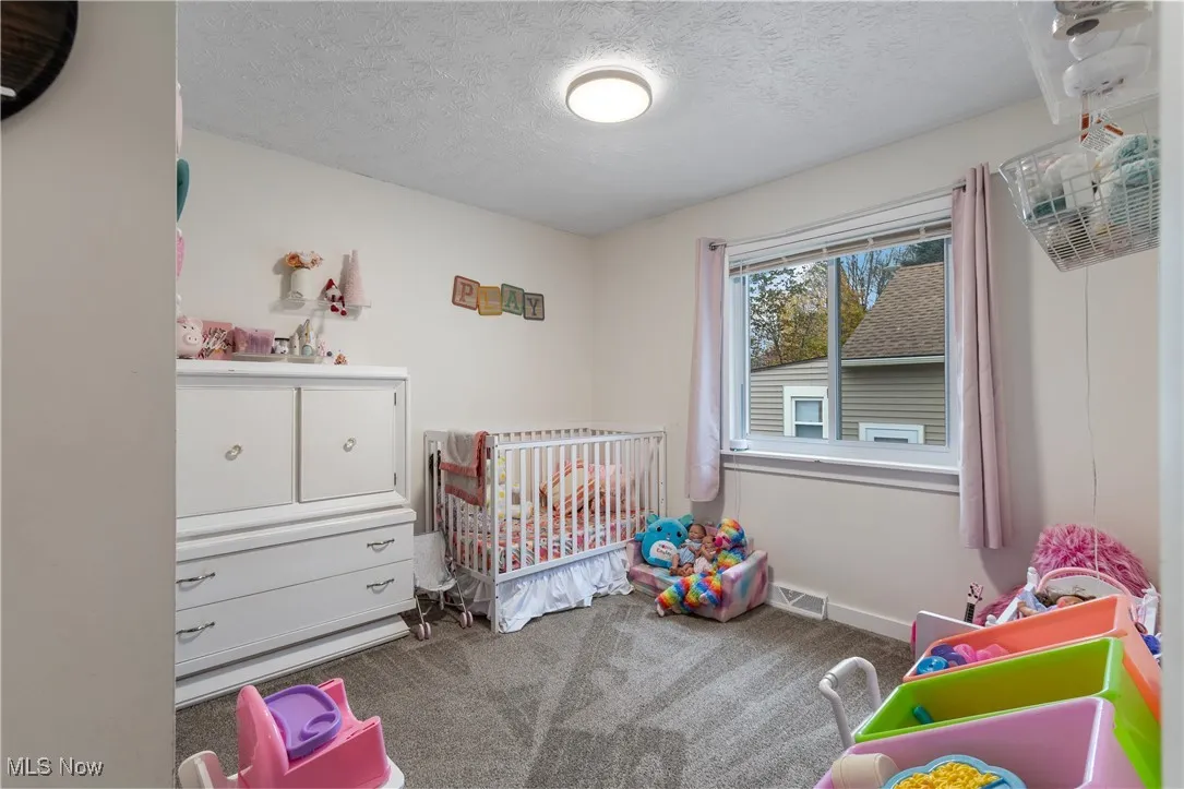 Bedroom featuring a textured ceiling, dark colored carpet, and a nursery area