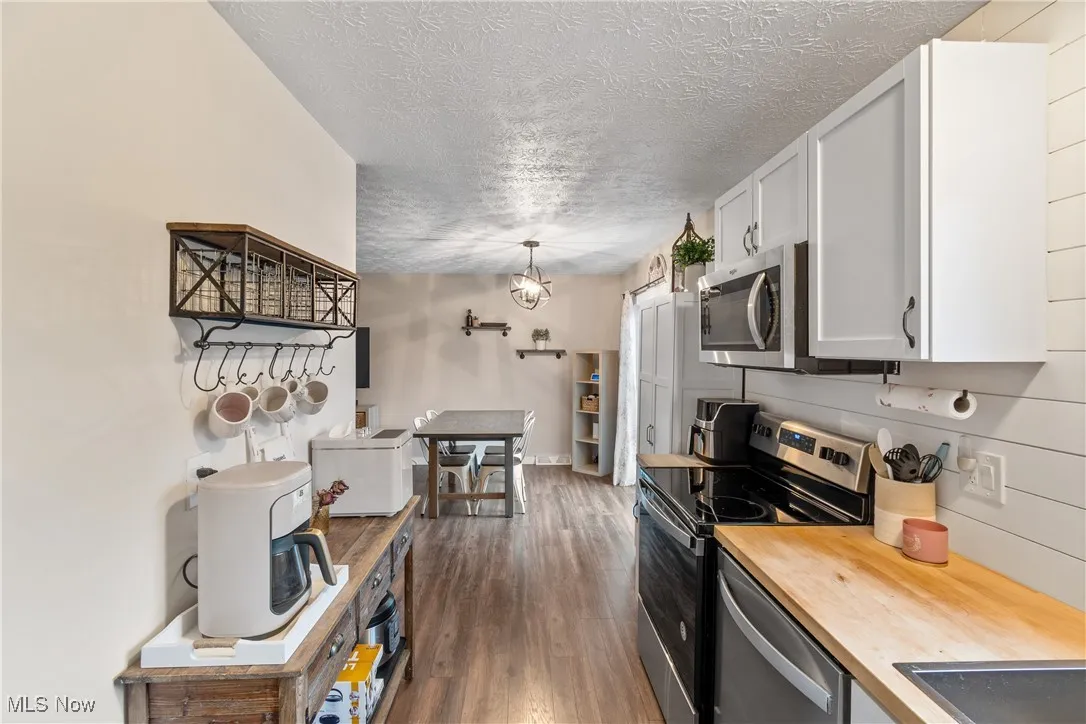Kitchen with appliances with stainless steel finishes, hanging light fixtures, dark wood-type flooring, a textured ceiling, and butcher block countertops