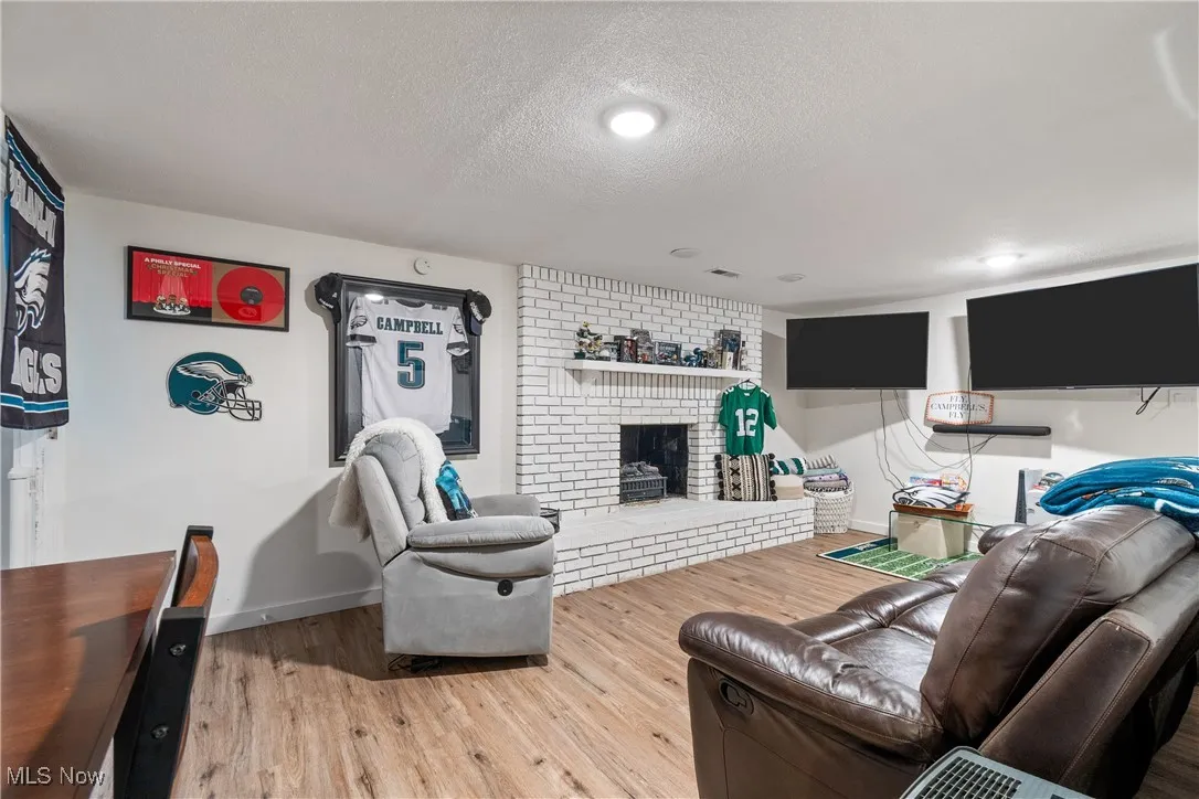 Living room with a textured ceiling, light wood-style floors, and a brick fireplace