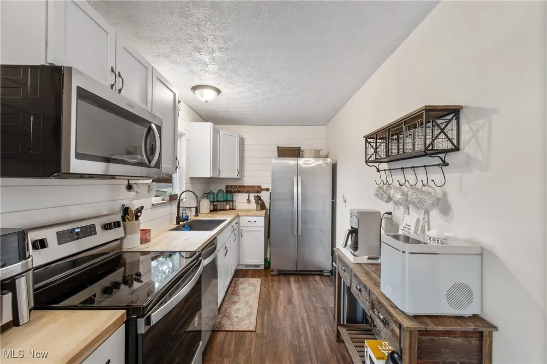 Kitchen featuring appliances with stainless steel finishes, dark wood-style flooring, white cabinetry, a textured ceiling, and butcher block countertops