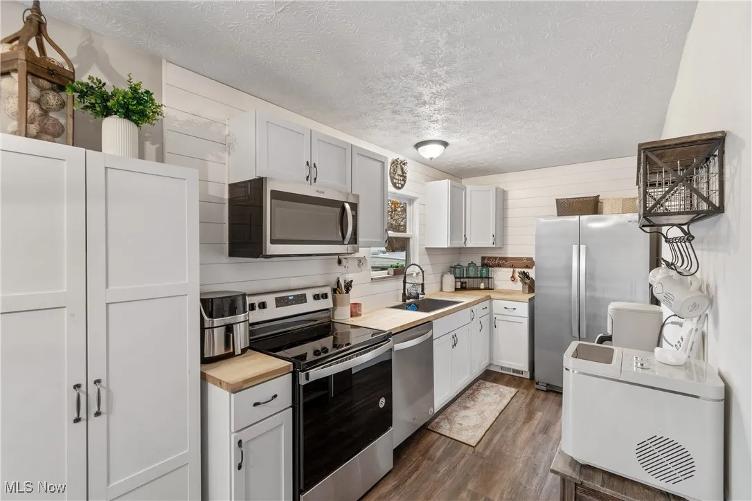 Kitchen with stainless steel appliances, dark wood-style floors, a textured ceiling, wood counters, and white cabinetry