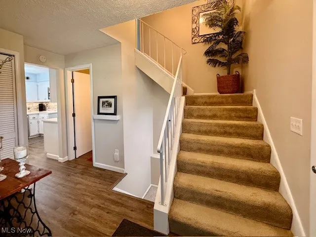 Stairway featuring a textured ceiling and wood finished floors.