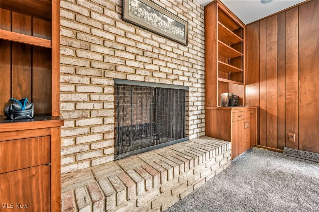 Detailed view of built in shelves, a brick fireplace, wooden walls, and carpet flooring