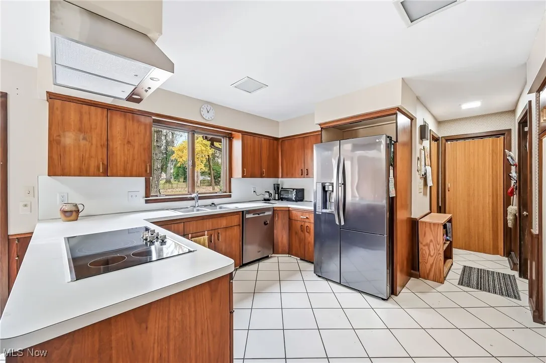Kitchen featuring walnut cabinetry, appliances with stainless steel finishes, exhaust hood, light countertops, and light tile floors