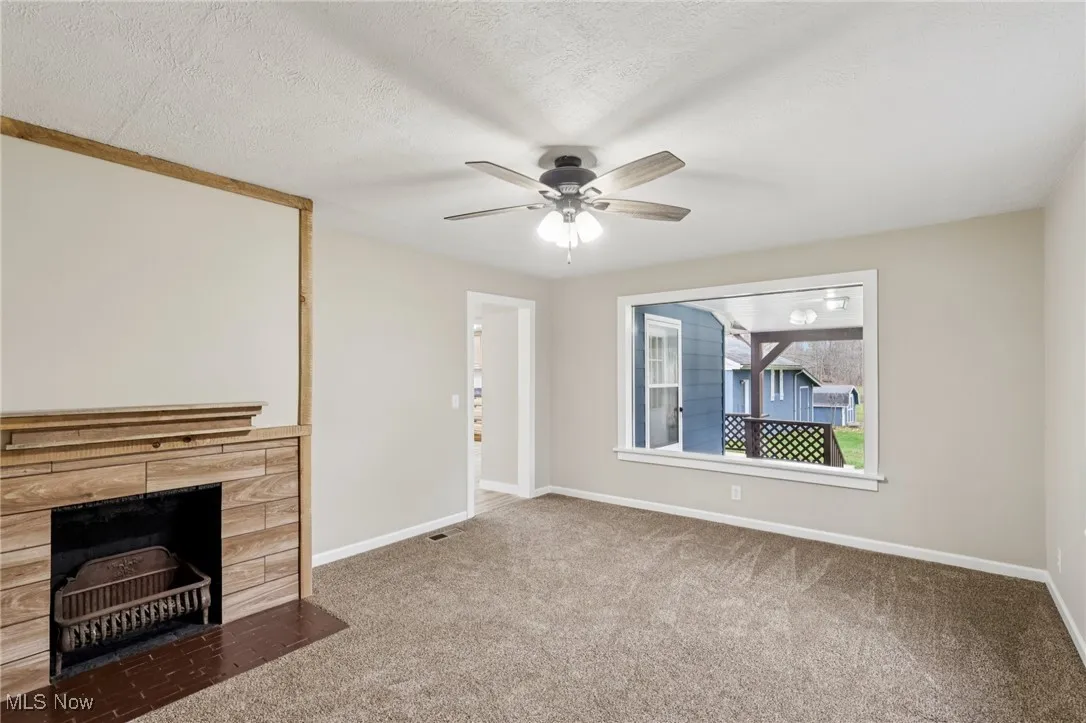 Unfurnished living room featuring a fireplace, carpet flooring, a textured ceiling, and ceiling fan