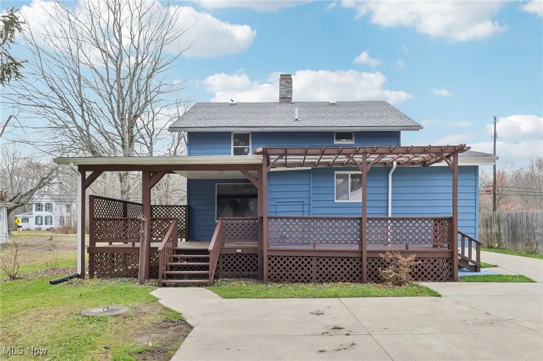 Rear view of house featuring a deck, a chimney, and roof with shingles