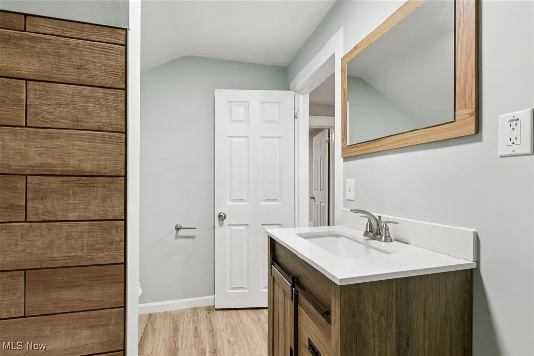 Bathroom featuring vanity, light wood-style floors, and vaulted ceiling