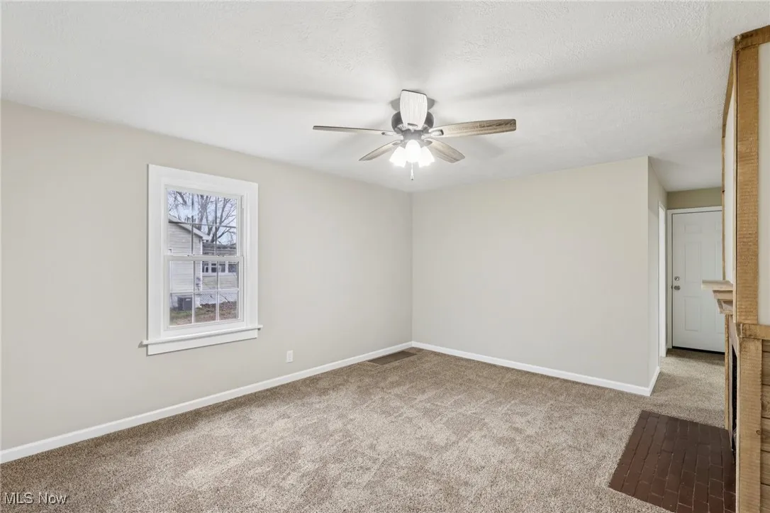 Empty room featuring light colored carpet, a ceiling fan, and a textured ceiling