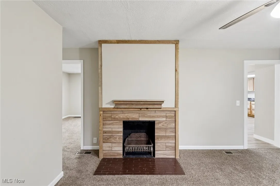 Unfurnished living room with carpet floors, a fireplace, ceiling fan, and a textured ceiling