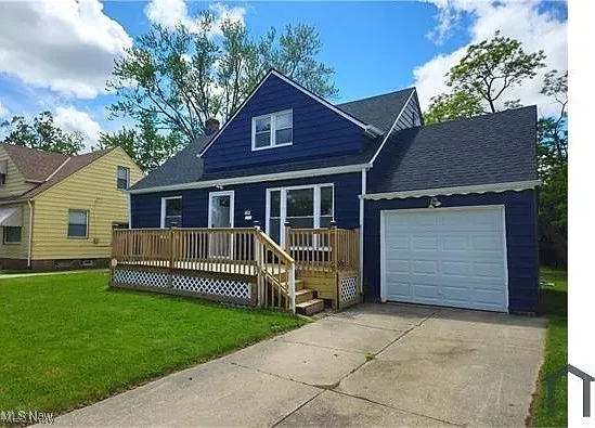 View of front of property featuring a garage, a deck, a front yard, driveway, and roof with shingles