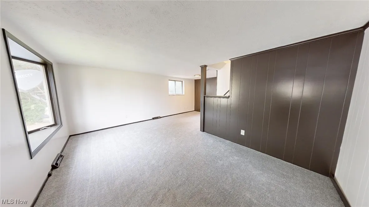 Spare room with wood walls, light colored carpet, and a textured ceiling