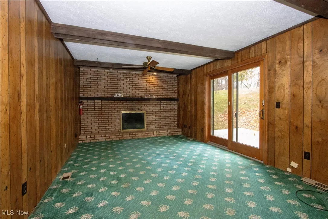 Unfurnished living room with wood walls, beam ceiling, carpet flooring, a brick fireplace, and a textured ceiling
