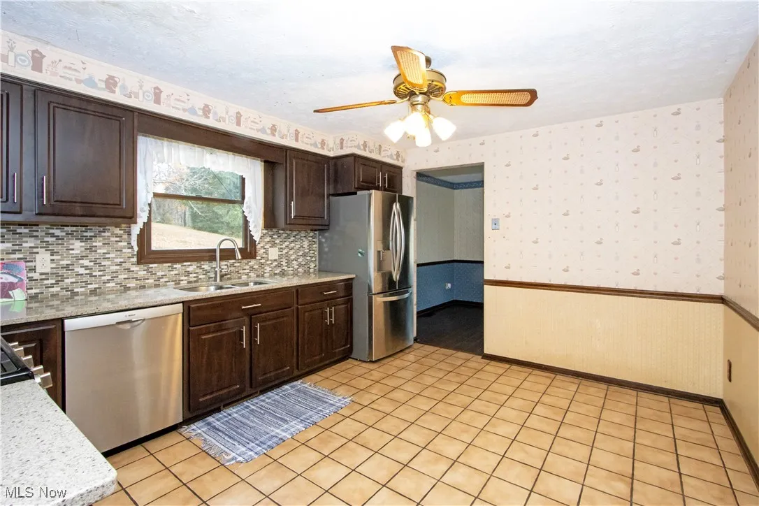 Kitchen featuring dark brown cabinetry, wallpapered walls, appliances with stainless steel finishes, a ceiling fan, and a wainscoted wall