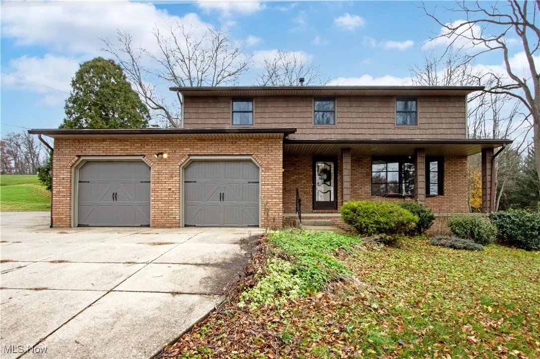 Traditional home with covered porch, driveway, an attached garage, brick siding, and a front yard