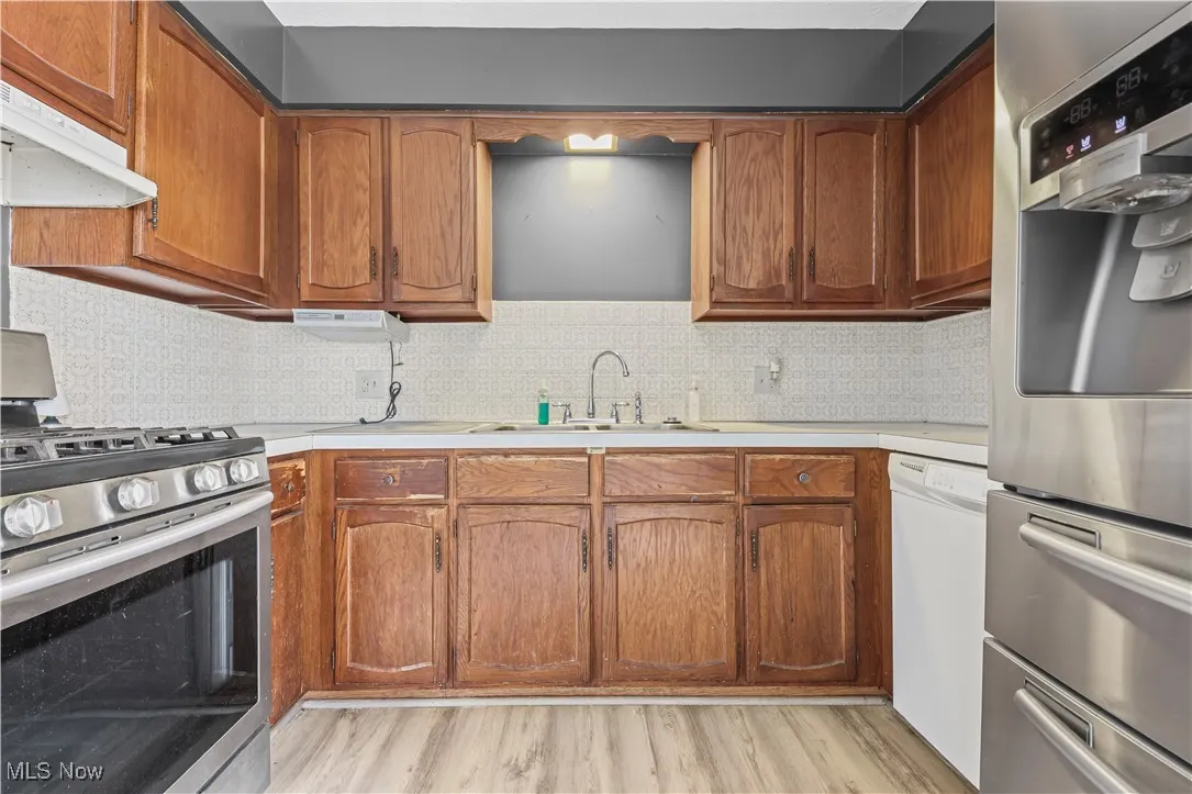 Kitchen with stainless steel appliances, light countertops, brown cabinetry, and tasteful backsplash