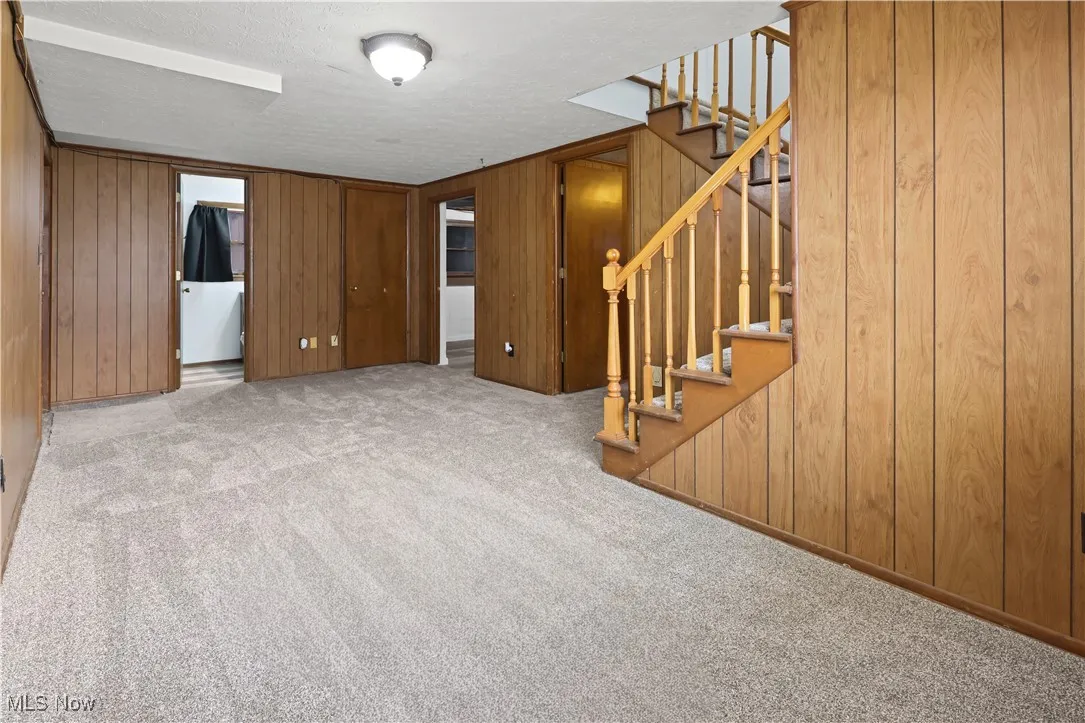 Unfurnished family room with wood walls, stairway, carpet floors, and a textured ceiling