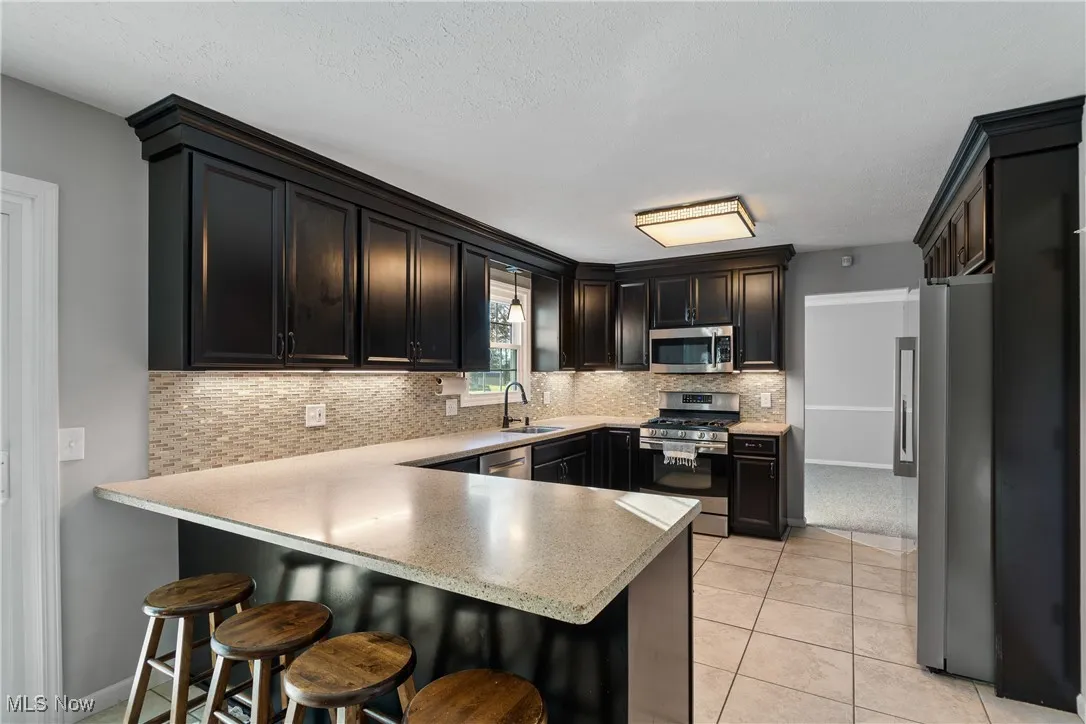 Kitchen featuring a kitchen bar, stainless steel appliances, a peninsula, decorative backsplash, and light tile patterned floors