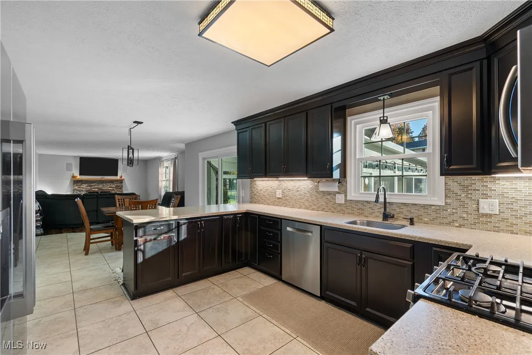 Kitchen with decorative backsplash, decorative light fixtures, light tile patterned floors, a textured ceiling, and appliances with stainless steel finishes