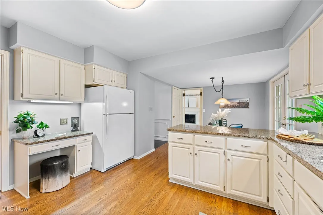 Kitchen featuring freestanding refrigerator, light stone counters, hanging light fixtures, light wood-style floors, and built in desk