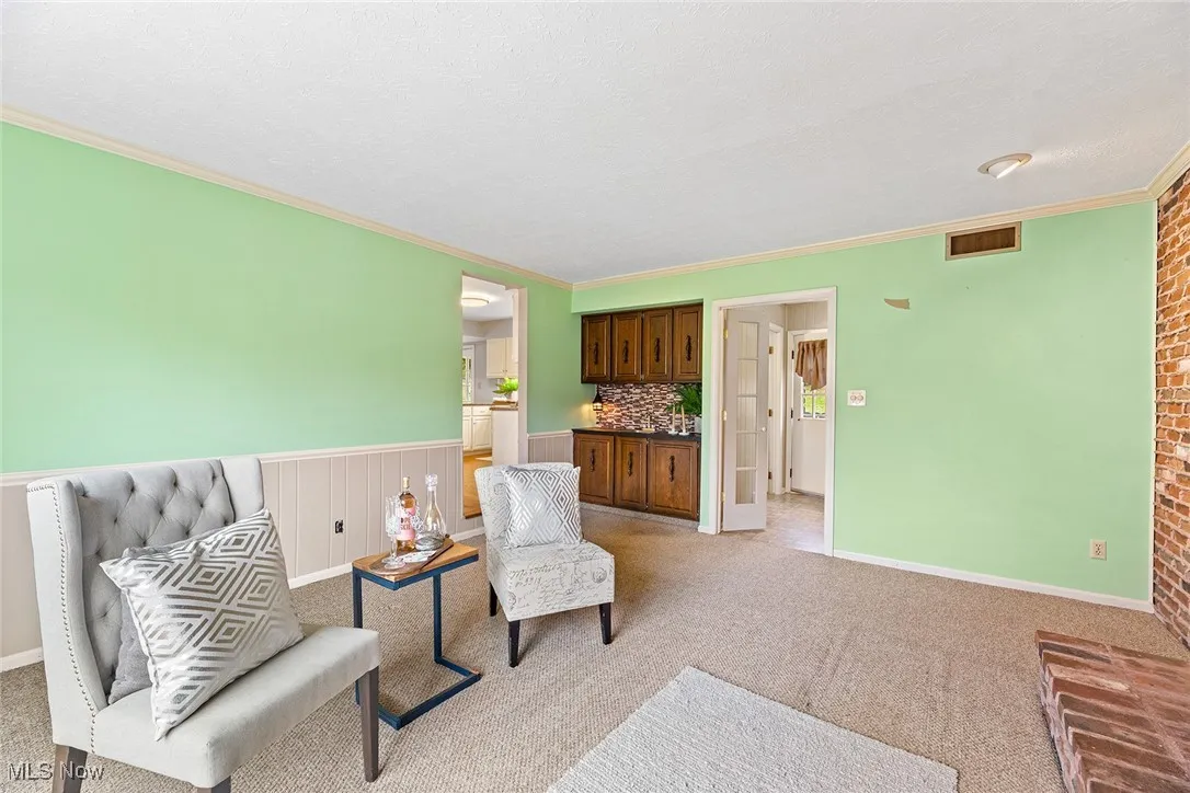 Living area with crown molding, a wainscoted wall, a textured ceiling, and light colored carpet