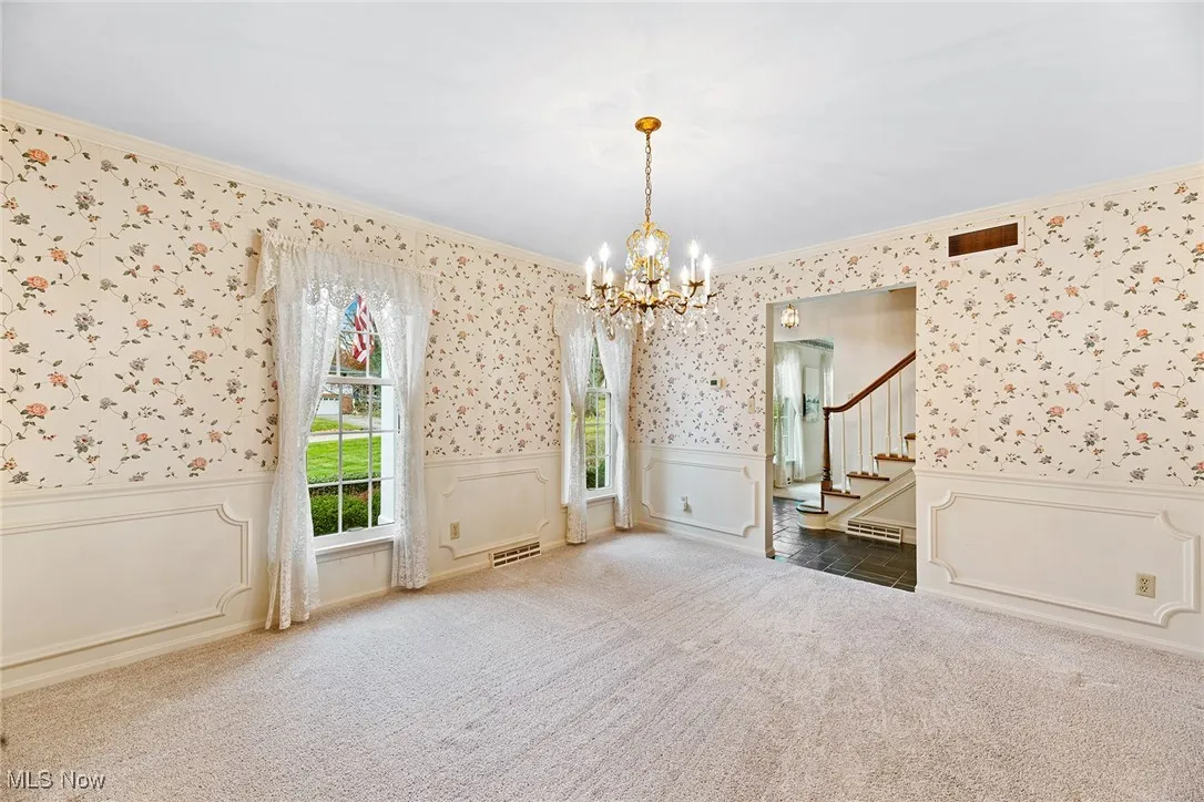 Unfurnished room featuring wainscoting, wallpapered walls, a chandelier, stairs, and a decorative wall