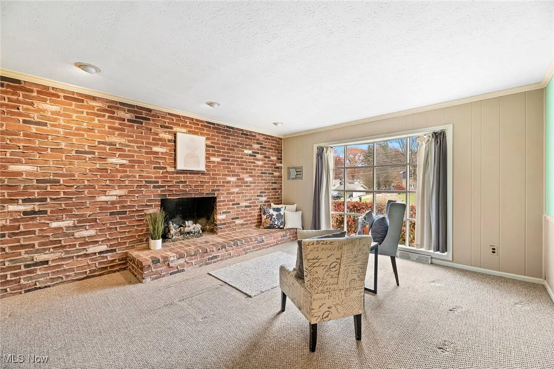 Carpeted living room featuring a brick fireplace, a textured ceiling, crown molding, wooden walls, and brick wall