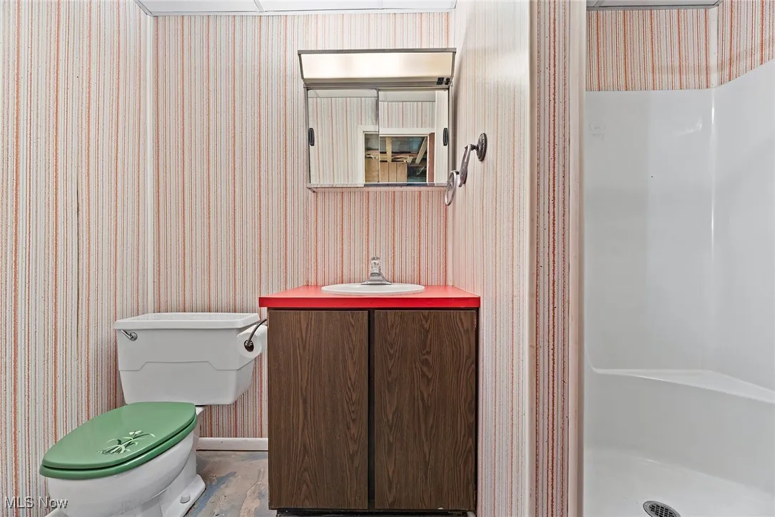 Bathroom featuring a stall shower, vanity, and wallpapered walls