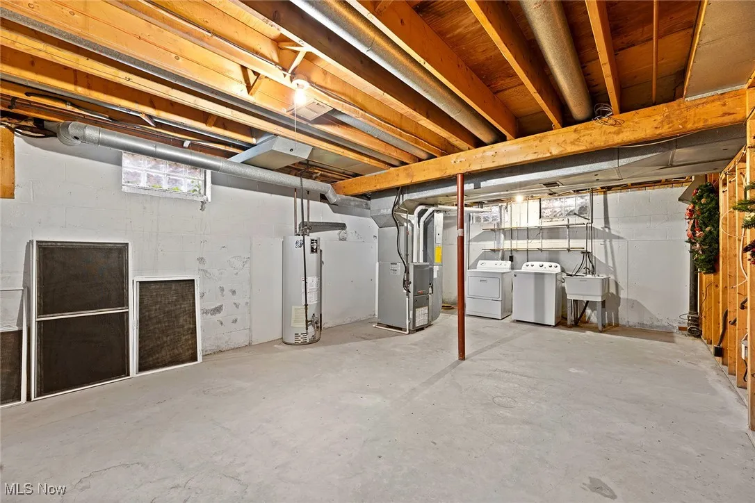 Basement featuring gas water heater, heating unit, and washing machine and dryer