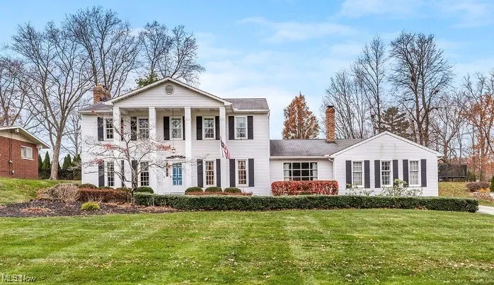 Neoclassical / greek revival house featuring a chimney, a front lawn, and a porch