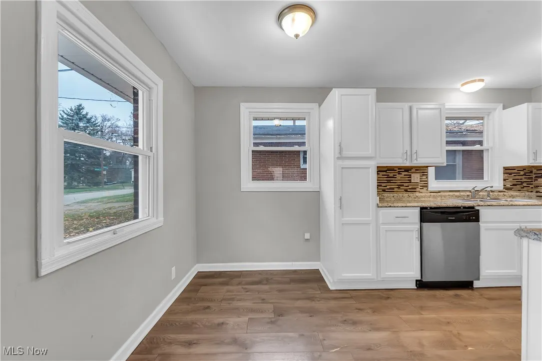 Kitchen featuring white cabinets, decorative backsplash, dishwasher, light stone countertops, and light wood-type flooring
