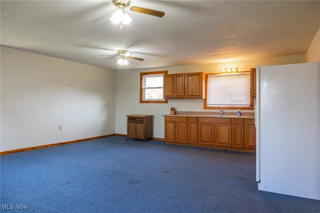 Kitchen with freestanding refrigerator, light countertops, brown cabinets, dark colored carpet, and a ceiling fan