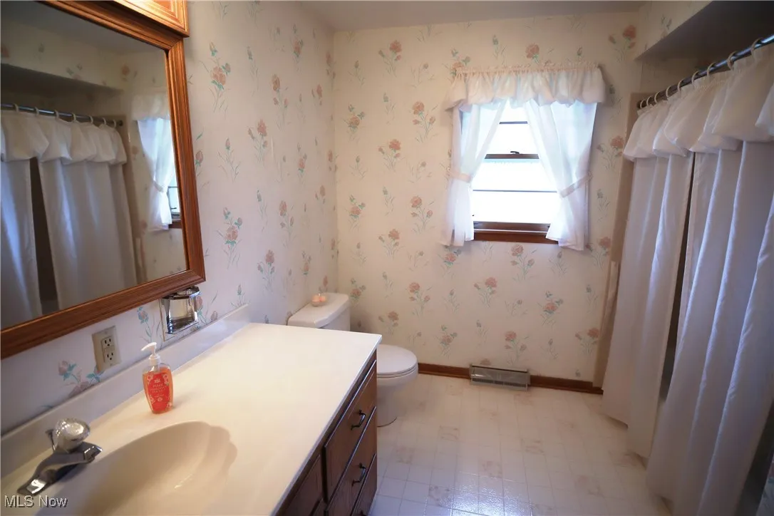 Bathroom featuring curtained shower, light flooring, wallpapered walls, and vanity