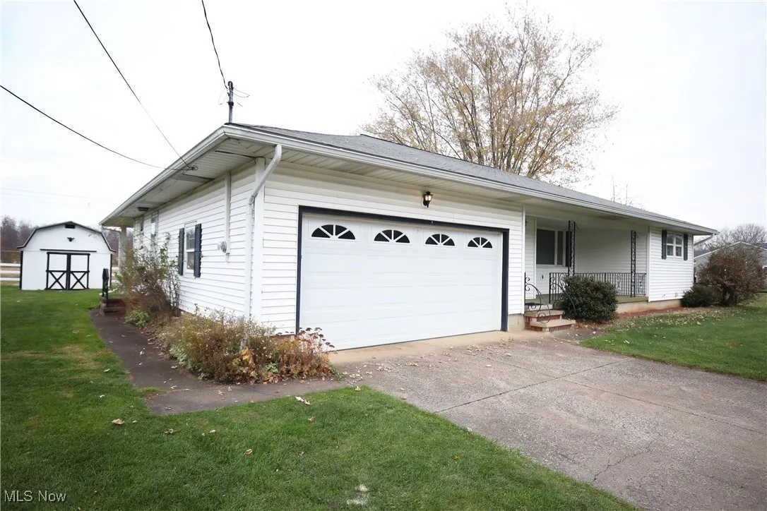 View of front of property featuring a front yard, driveway, a garage, covered porch, and a shed