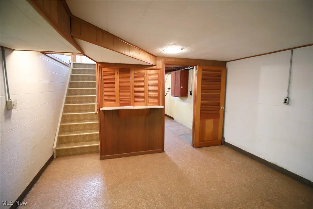 Finished basement featuring stairs, light flooring, concrete block wall, and wooden walls