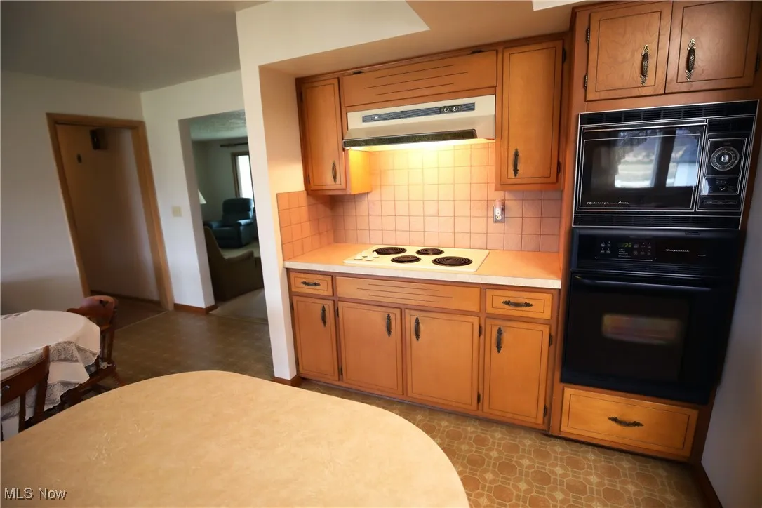 Kitchen featuring black appliances, light countertops, under cabinet range hood, light floors, and decorative backsplash