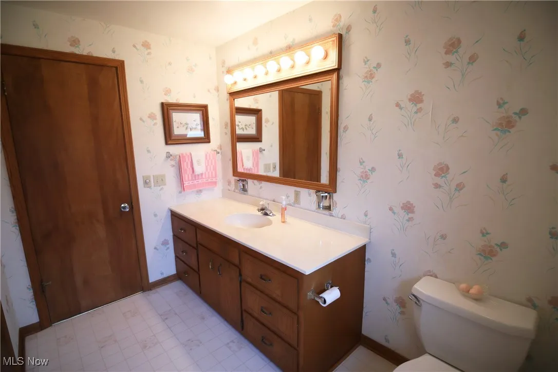 Half bath featuring vanity, wallpapered walls, and light floors
