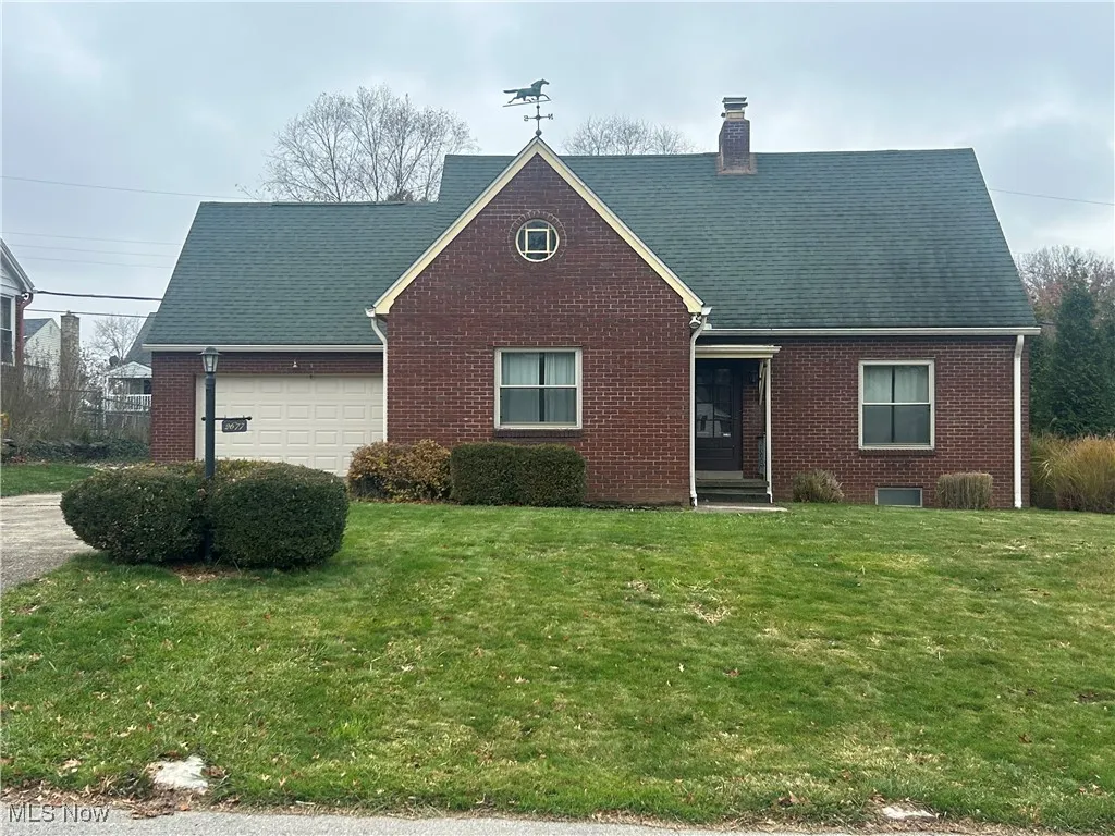 View of front of home featuring brick siding, a front lawn, a chimney, and an attached garage