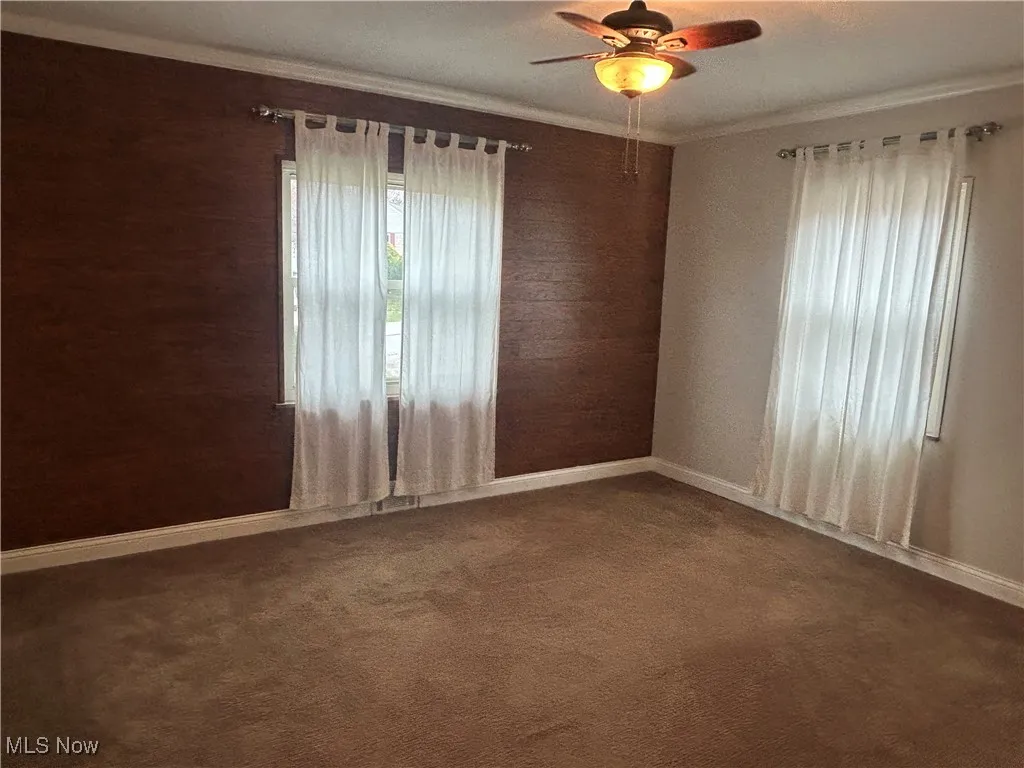 Unfurnished room with ornamental molding, a ceiling fan, dark carpet, and wood walls