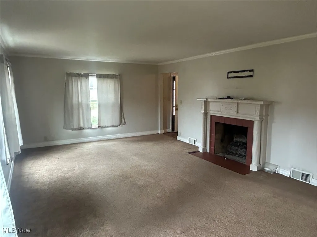 Unfurnished living room featuring crown molding, a tiled fireplace, and carpet flooring
