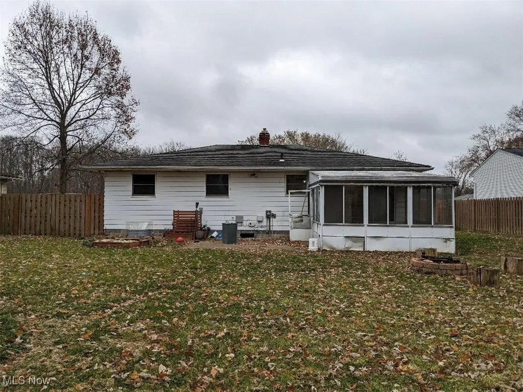 Rear view of property with a fenced backyard, a sunroom, and a chimney